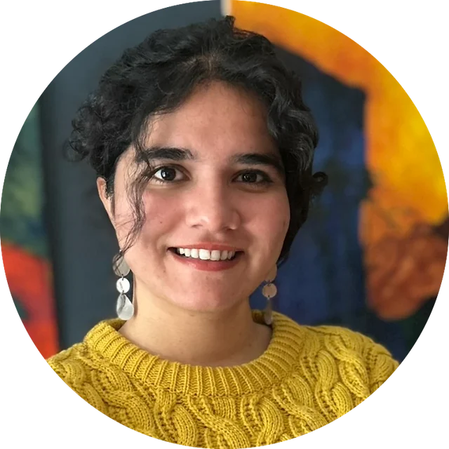 Sumairha, smiling, in a mustard cable-knit sweater in front of a colourful painting